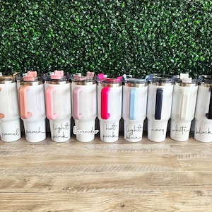 May include: A row of 10 white stainless steel tumblers with different coloured handles. The handles are lime green, camel, peach, light pink, lavender, hot pink, light blue, navy, white, and red.