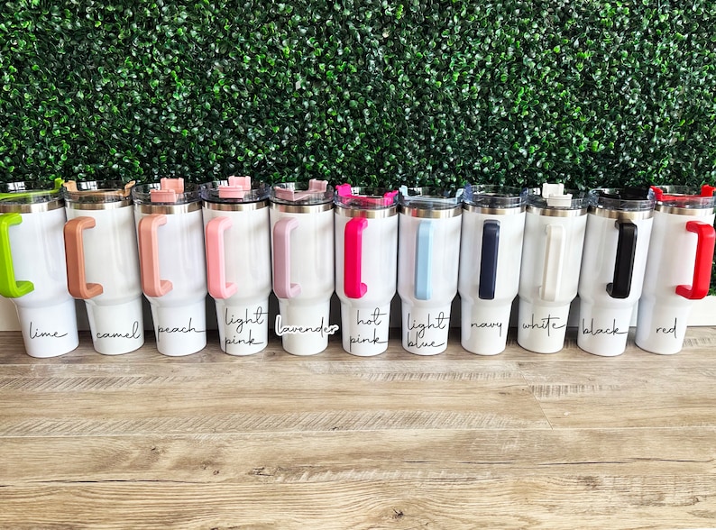 May include: A row of 10 white stainless steel tumblers with different coloured handles. The handles are lime green, camel, peach, light pink, lavender, hot pink, light blue, navy, white, and red.