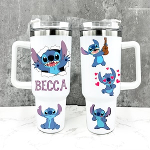 May include: Two white stainless steel travel mugs featuring a blue Stitch character from the Disney film Lilo & Stitch. One mug shows Stitch peeking out of a hole with the name "BECCA" printed below. The other mug depicts Stitch playing a ukulele, Stitch with hearts around his head, and Stitch with his arms crossed.