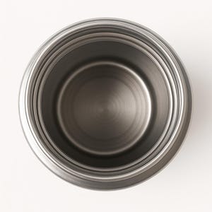 May include: A stainless steel pot, viewed from above, with a circular design. The pot has a shiny, metallic finish and a simple, modern aesthetic. The interior is a darker shade of gray, with concentric circles.