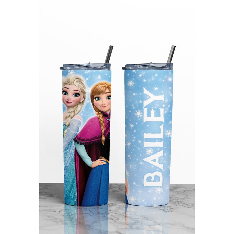K&ouml;nnte beinhalten: Zwei Edelstahlbecher mit Deckel und Strohhalmen. Ein Becher hat einen blauen Hintergrund mit wei&szlig;en Schneeflocken und den Namen "BAILEY" in wei&szlig;. Der andere Becher zeigt ein Bild von Elsa und Anna aus dem Film Frozen.