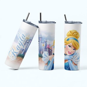 May include: A white stainless steel tumbler with a blue and pink Cinderella design. The tumbler has a straw and the name "Rayla" is written on the side.