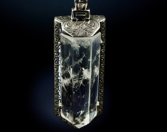 May include: A silver pendant necklace with a clear crystal encased in an ornate silver frame. The crystal has a cloudy, white appearance.