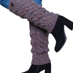May include: A pair of gray cable-knit leg warmers with flecks of color, worn over blue jeans and black heeled boots. The leg warmers have a button detail at the top and a textured, patterned design.
