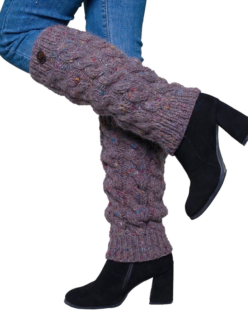 May include: A pair of gray cable-knit leg warmers with flecks of color, worn over blue jeans and black heeled boots. The leg warmers have a button detail at the top and a textured, patterned design.