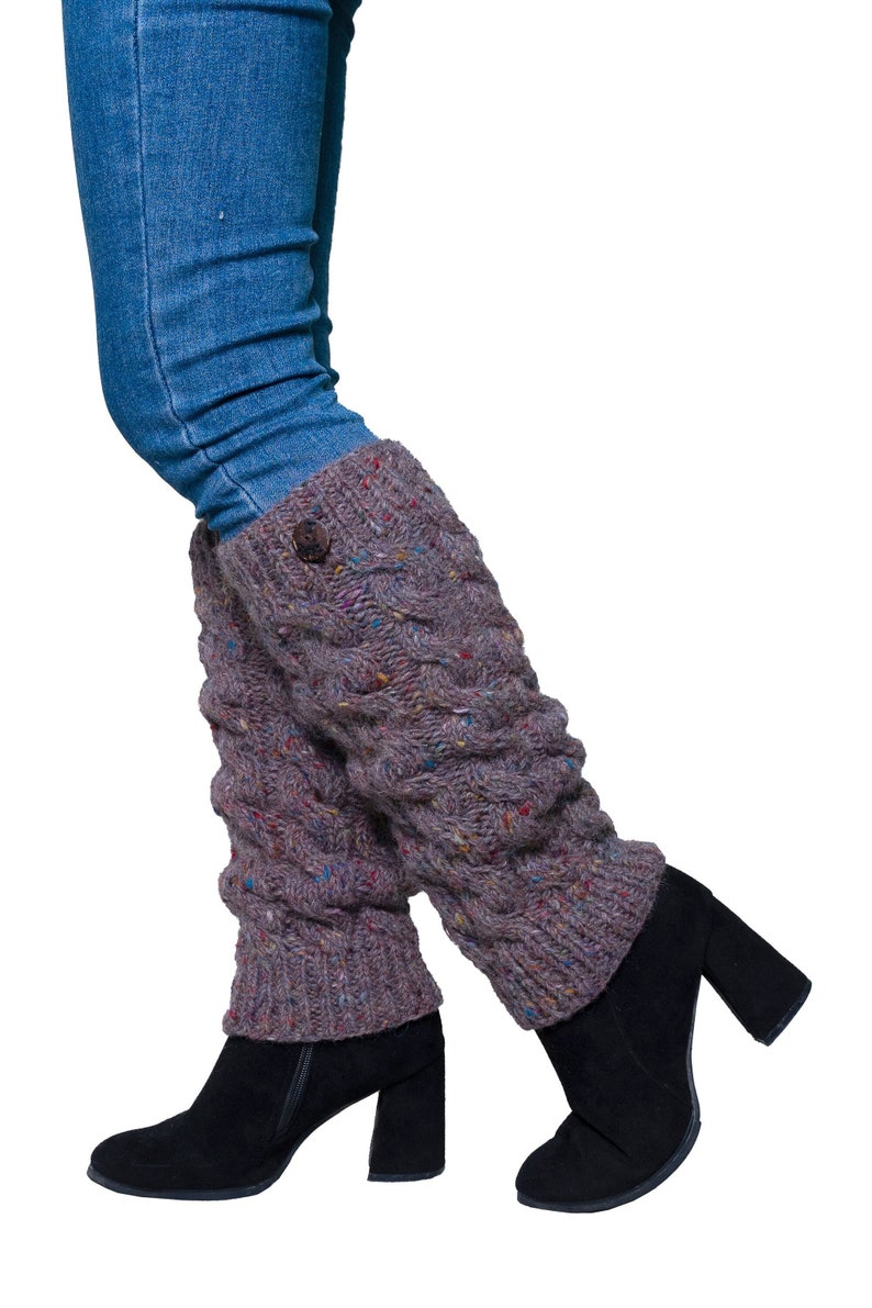 May include: A pair of gray cable-knit leg warmers with a button detail, worn over black heeled boots and blue jeans. The leg warmers have flecks of color throughout the knit.