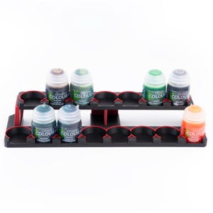 May include: A black plastic paint pot holder with red accents. The holder has two tiers and is filled with small bottles of paint. The bottles are labeled "Citadel Colour" and have different shades of green and brown paint.