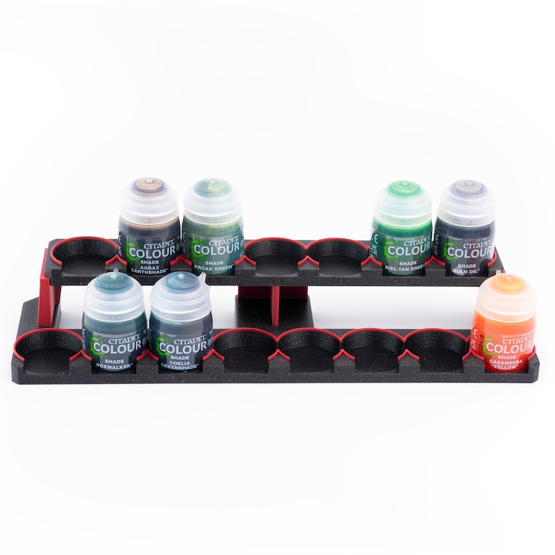 May include: A black plastic paint pot holder with red accents. The holder has two tiers and is filled with small bottles of paint. The bottles are labeled "Citadel Colour" and have different shades of green and brown paint.