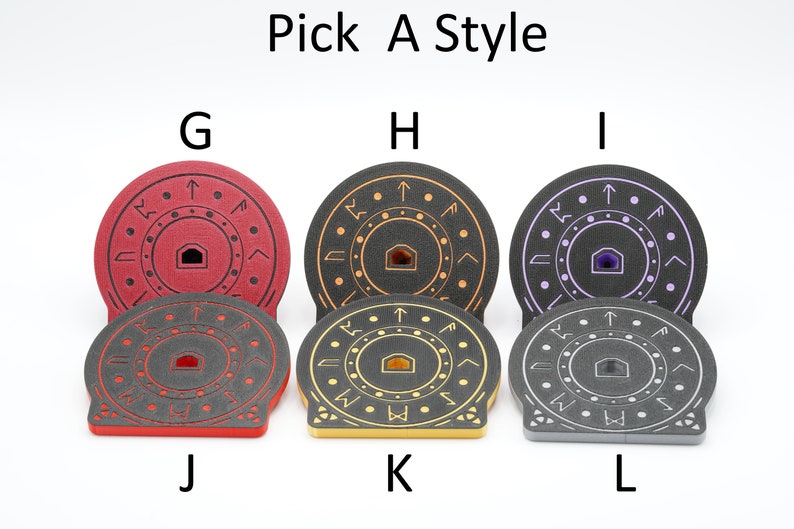 K&ouml;nnte beinhalten: Sechs runde, schwarze Schaumstoffuntersetzer mit verschiedenen farbigen Mittelpunkten. Die Untersetzer haben ein Design aus einem Kreis mit einem kleineren Kreis in der Mitte. Die Mittelpunkte sind rot, gold, lila, rot, gold und grau. Die Untersetzer sind mit den Buchstaben G, H, I, J, K und L beschriftet.
