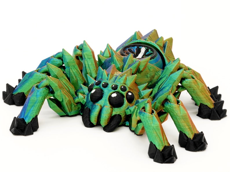 May include: A 3D printed, iridescent green spider with black eyes and legs. The spider has a crystalline texture and is posed in a crawling position.