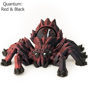 May include: A red and black 3D printed spider with a large, round eye in the center of its head. The spider has eight legs and a spiky body. The text "Quantum: Red & Black" is visible in the top left corner of the image.