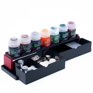 May include: A black plastic paint organiser with eight small paint bottles, a compartment for paint brushes, and a compartment for small metal discs. The paint bottles are labelled "Citadel Colour" and have different shades of paint.