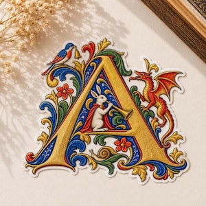 May include: A decorative sticker featuring a large, gold-colored letter A adorned with intricate blue, green, and red floral scrollwork. A white rabbit in a red cape plays a trumpet inside the letter, accompanied by a red dragon, a blue bird, and a snail.