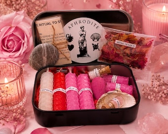 May include: A black metal tin containing four honeycomb-textured candles in white, red, and pink, a small pink sphere, two glass vials with corks, a bag of dried rose petals, a grey stone, and a circular sticker featuring a statue and the text APHRODITE.