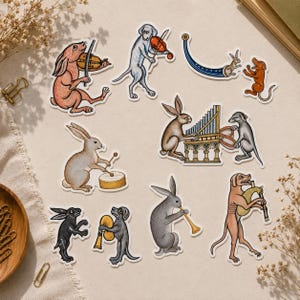 May include: A collection of stickers featuring medieval-style illustrations of rabbits and dogs playing musical instruments, including a violin, a drum, a pipe organ, a trumpet, and bagpipes, rendered in muted earth tones and detailed line work.