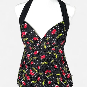 May include: A black halter top with a cherry print. The top features a pattern of red cherries, green leaves, and white polka dots. The halter straps and neckline are solid black.