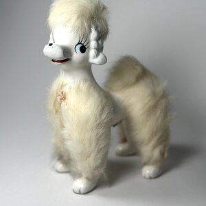 May include: A vintage white ceramic poodle figurine with fluffy cream-colored fur accents. The poodle has black eyes, long eyelashes, and a red mouth. The figurine is a decorative item.