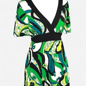 May include: A sleeveless dress with a V-neck and a black waistband. The dress has a vibrant pattern of green, white, and black abstract shapes and floral accents. The hemline and neckline are trimmed in black.