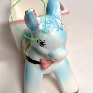 May include: A ceramic donkey planter in shades of blue, white, and pink. The donkey has a bow tie and a black collar. The planter has a rectangular opening for plants.
