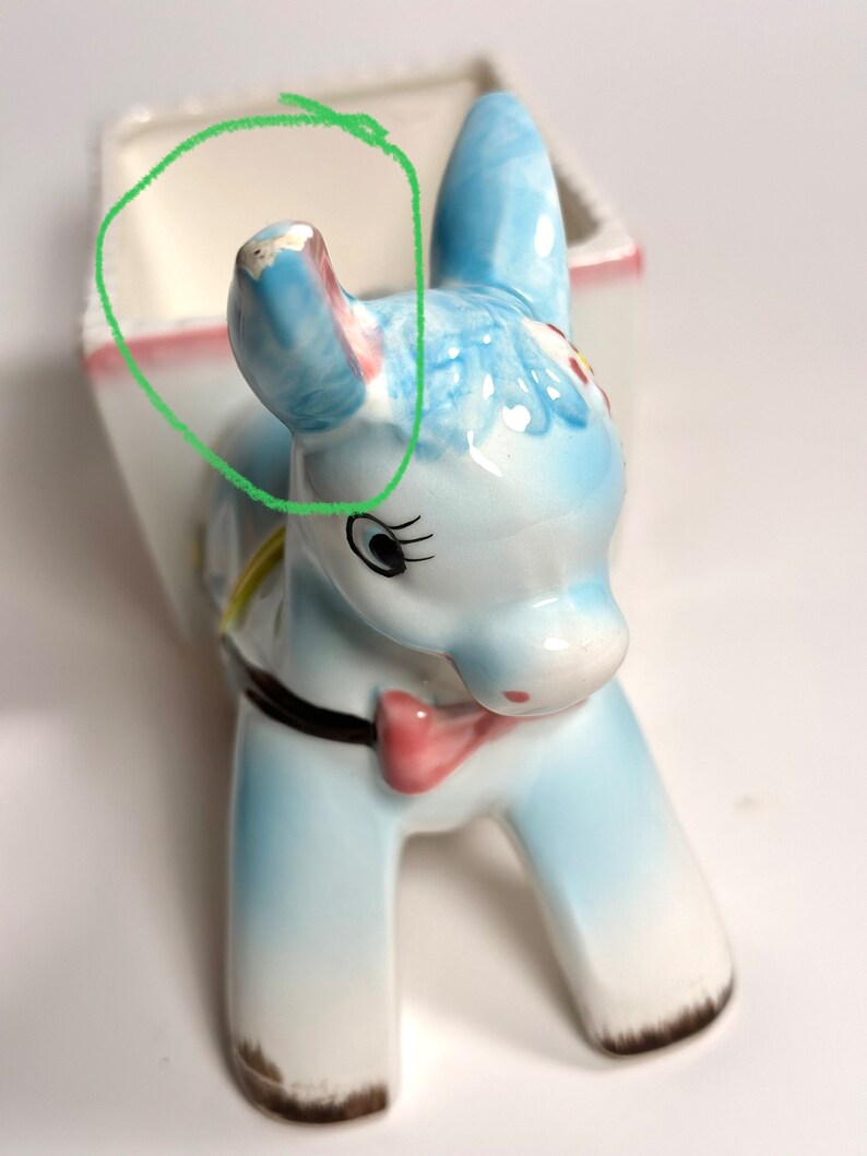May include: A ceramic donkey planter in shades of blue, white, and pink. The donkey has a bow tie and a black collar. The planter has a rectangular opening for plants.
