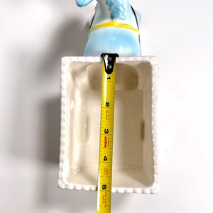 May include: A light blue ceramic donkey head planter with a white rectangular planter. The planter is approximately 5 inches long. The donkey has a yellow harness and black bridle. The planter has a white rim with a textured design.