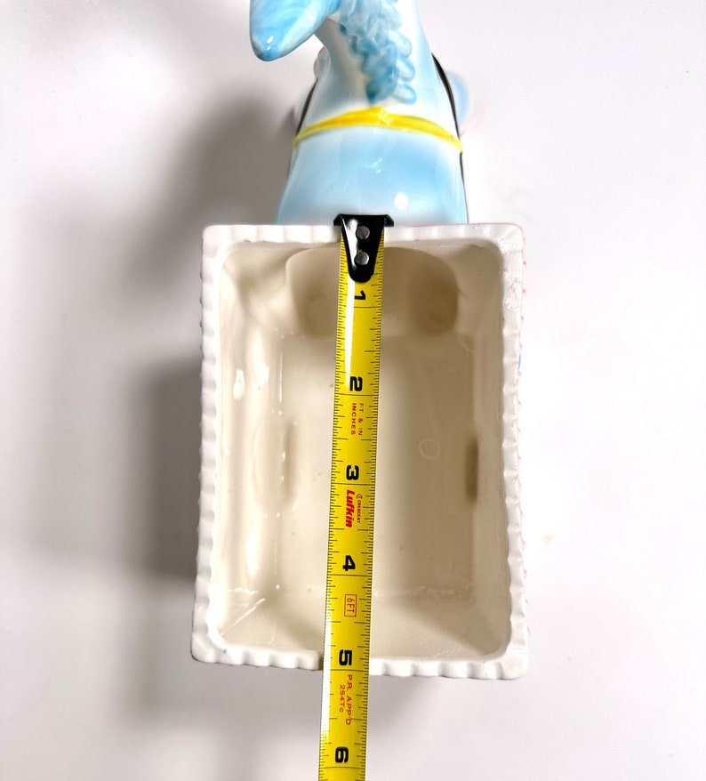 May include: A light blue ceramic donkey head planter with a white rectangular planter. The planter is approximately 5 inches long. The donkey has a yellow harness and black bridle. The planter has a white rim with a textured design.