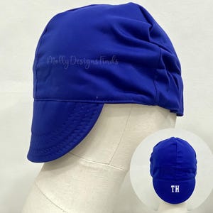May include: A solid royal blue welding cap with a short, rounded brim and a smooth fabric finish. The cap features the text Molly Designs Finds in a light script font. A smaller inset shows the back of the cap with the white embroidered letters TH.
