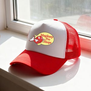 May include: A red and white trucker hat with a red brim and a white front panel. The front panel features a graphic of a red fish with the text "Magikarp Pro Shops" in a yellow oval.