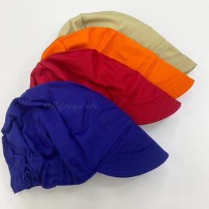 May include: A set of four fabric caps in blue, red, orange, and beige. Each cap features a rounded crown with gathered fabric at the back and a short, stiffened brim with visible stitching. The text Molly Designs Finds is printed on the blue cap.