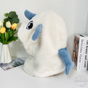 May include: White plush hooded animal head with blue ears and tail. The head has large black eyes and a white, fluffy texture.