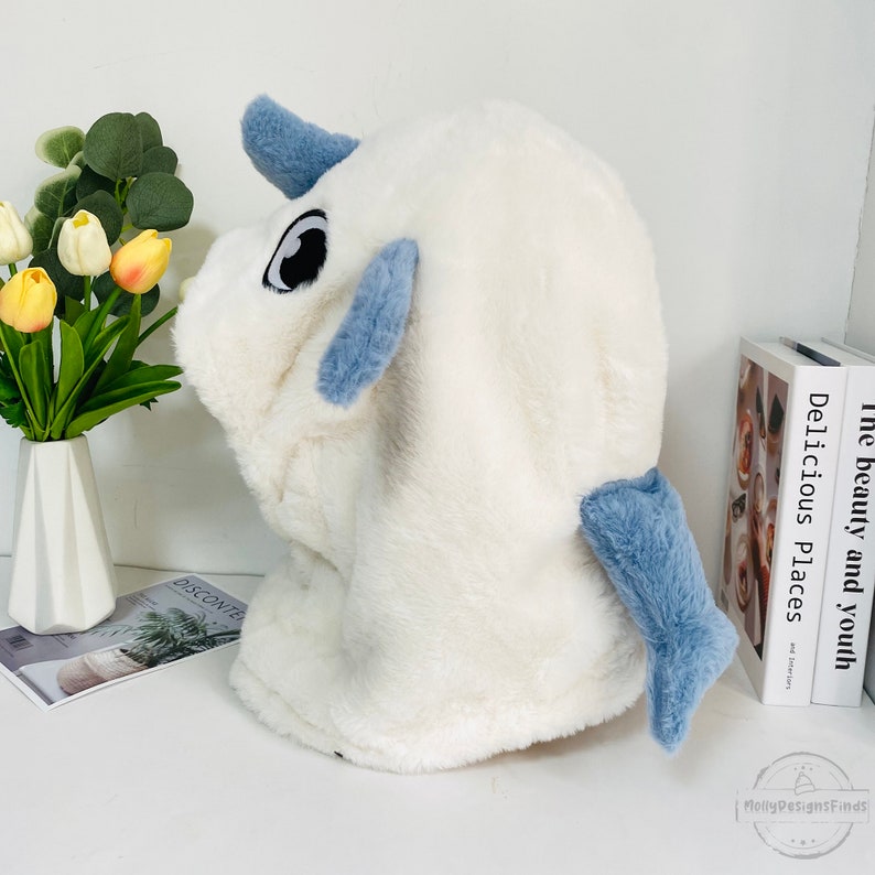 May include: White plush hooded animal head with blue ears and tail. The head has large black eyes and a white, fluffy texture.