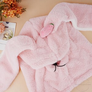 May include: A pink plush hooded jacket with a small pink plush strawberry attached to the hood.