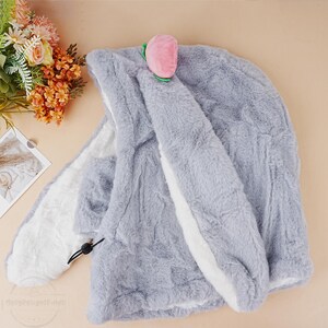 May include: A gray plush hooded blanket with a white trim and a pink peach-shaped applique on the hood.