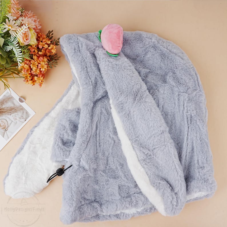 May include: A gray plush hooded blanket with a white trim and a pink peach-shaped applique on the hood.