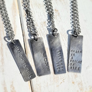 May include: Four silver necklaces with rectangular pendants. The pendants have different inscriptions: "AMOR", "NORT MEMORIAS", "VII.XII.MCMXCIX", and "CHAOS IS A FRIEND OF MINE".