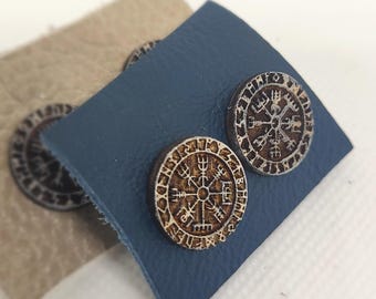 May include: A pair of wooden earrings with a circular design featuring a compass with runes around the edge. The earrings are on a blue and beige background.