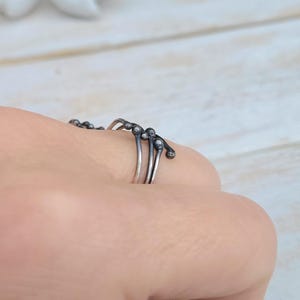 Puede incluir: Un conjunto de anillos de plata con un dise&ntilde;o &uacute;nico. Cada anillo presenta una banda delgada con peque&ntilde;os acentos redondos y oscuros. Los anillos se llevan en un dedo, mostrando su estilo delicado y art&iacute;stico. Los anillos probablemente est&aacute;n hechos de plata de ley.