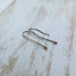 May include: A pair of silver hoop earrings with rose gold accents. The earrings are simple and delicate, and they would make a great gift for any occasion.