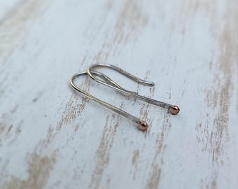 May include: A pair of silver hoop earrings with rose gold accents. The earrings are simple and delicate, and they would make a great gift for any occasion.