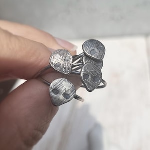 May include: A set of five silver rings with a skull design. Each ring has a textured surface and two small white dots for eyes.
