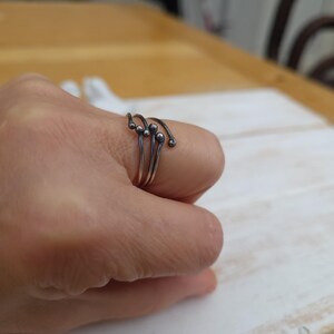 Puede incluir: Un anillo plateado con un dise&ntilde;o &uacute;nico. El anillo presenta m&uacute;ltiples bandas que se curvan y terminan con peque&ntilde;os adornos redondos. La joya se lleva en un dedo, mostrando su est&eacute;tica minimalista y moderna.