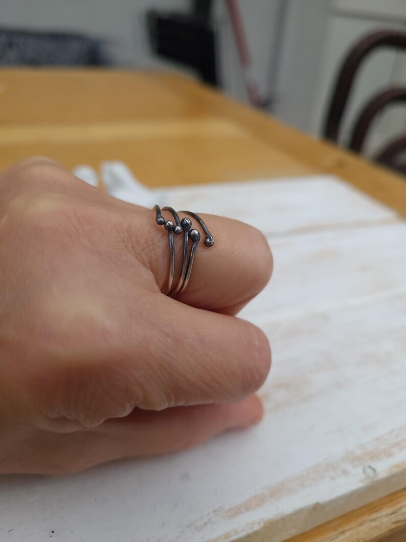 Puede incluir: Un anillo plateado con un dise&ntilde;o &uacute;nico. El anillo presenta m&uacute;ltiples bandas que se curvan y terminan con peque&ntilde;os adornos redondos. La joya se lleva en un dedo, mostrando su est&eacute;tica minimalista y moderna.