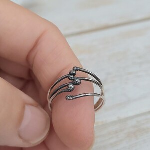 Puede incluir: Un anillo de plata con un dise&ntilde;o &uacute;nico de cerillas. El anillo presenta tres bandas curvas, cada una con un detalle de cabeza de cerilla. El anillo se lleva en un dedo, mostrando su dise&ntilde;o intrincado y art&iacute;stico. El anillo es una joya.
