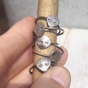May include: A set of five silver rings with alien face designs. The rings are stacked on a wooden dowel.