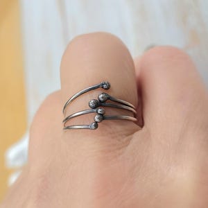 Puede incluir: Un anillo plateado con un dise&ntilde;o &uacute;nico. El anillo presenta cuatro bandas curvas, cada una con una peque&ntilde;a bola texturizada en el extremo, que se asemejan a cerillas. El anillo se lleva en un dedo, mostrando su estilo art&iacute;stico e inusual.