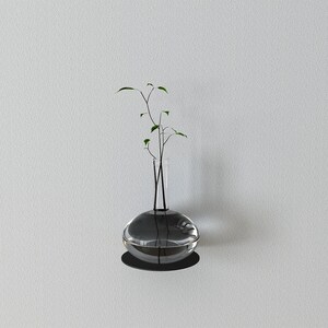May include: A clear glass vase with a round base and a narrow neck, filled with water and a small green plant with thin stems.