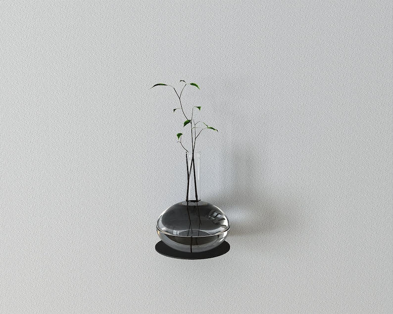 May include: A clear glass vase with a round base and a narrow neck, filled with water and a small green plant with thin stems.