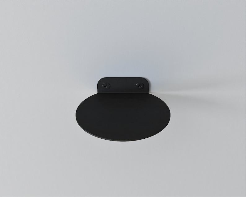 May include: A black metal shelf with rounded edges, mounted to a white wall.