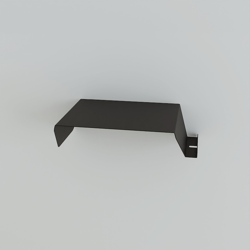 A black metal shelf with a minimalist design. The shelf has a flat top and a downward-sloping front edge. A small, vertical support with a rectangular cutout is on the right side. The shelf is designed to be mounted on a wall.