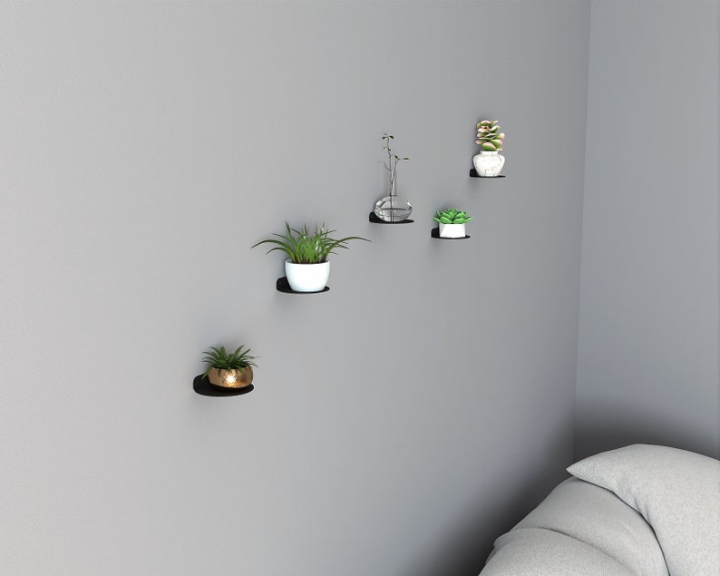 May include: Five black floating shelves mounted on a gray wall, each holding a potted plant. The plants include succulents, a small tree, and a vase with greenery.